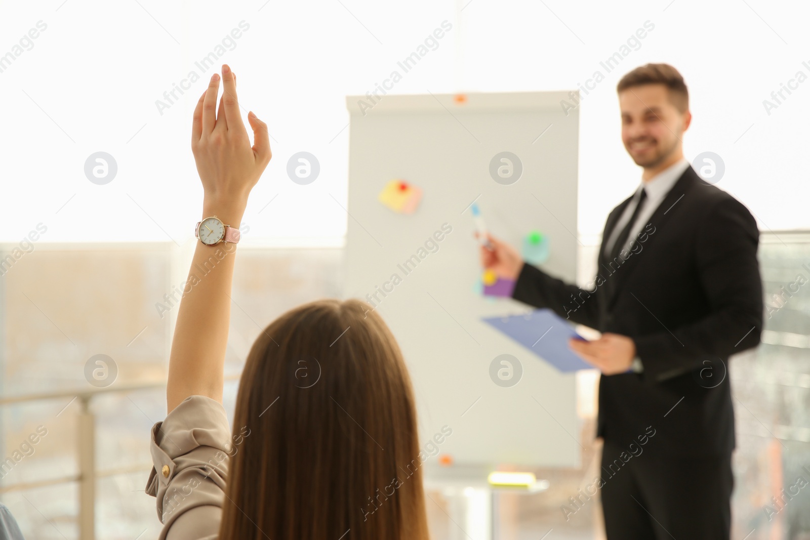 Photo of Young woman raising hand to ask question at business training indoors, closeup