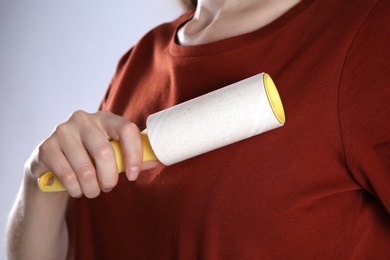 Woman cleaning red t-shirt with lint roller on grey background, closeup