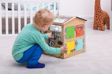 Photo of Cute little boy playing with busy board house on floor at home