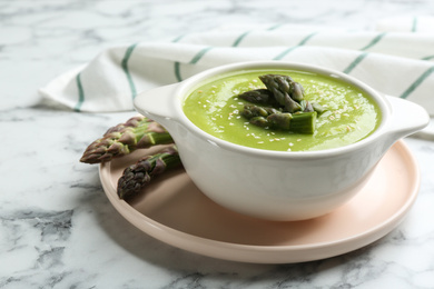 Photo of Delicious asparagus soup served on white marble table