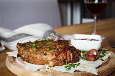 Photo of Delicious grilled pork chop served on wooden table indoors