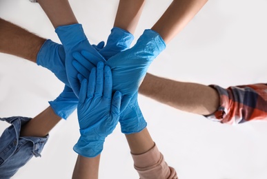 Group of people in blue medical gloves stacking hands on light background, bottom view