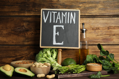 Photo of Small chalkboard with phrase Vitamin E and different products on wooden background