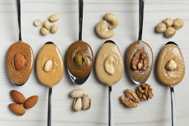 Photo of Tasty nut butters in spoons and raw nuts on white wooden table, flat lay