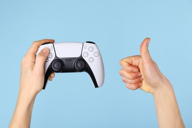 Woman with game controller showing thumbs up on light blue background, closeup