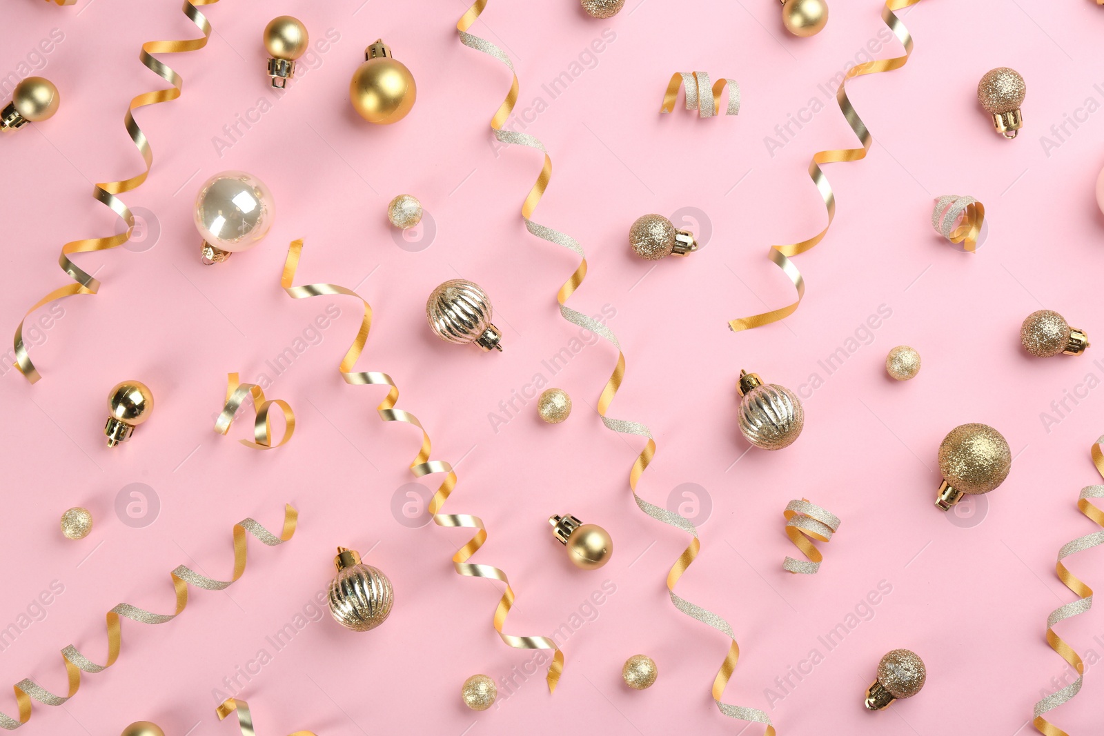 Photo of Shiny serpentine streamers and Christmas balls on pink background, flat lay