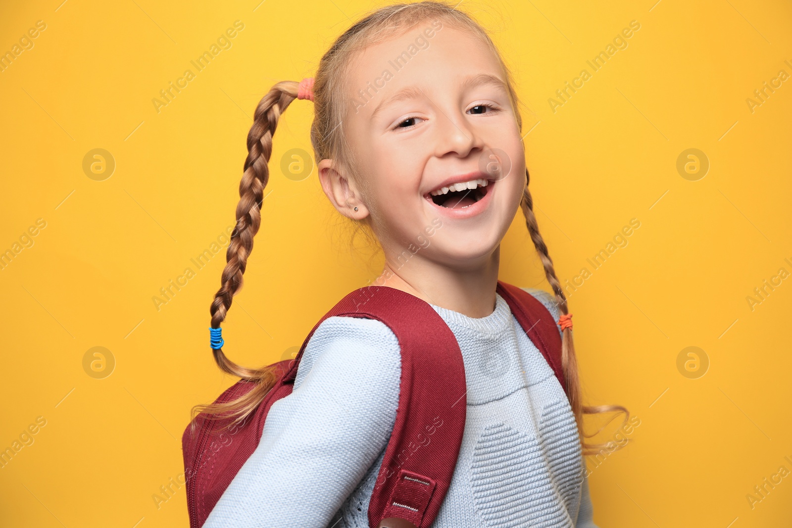 Photo of Cute little girl with backpack on yellow background