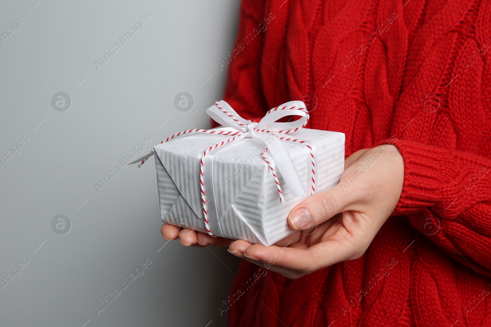 Photo of Woman holding white Christmas gift box on grey background, closeup