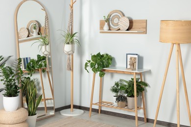 Stylish room interior with wooden furniture, houseplants and full length mirror near white wall