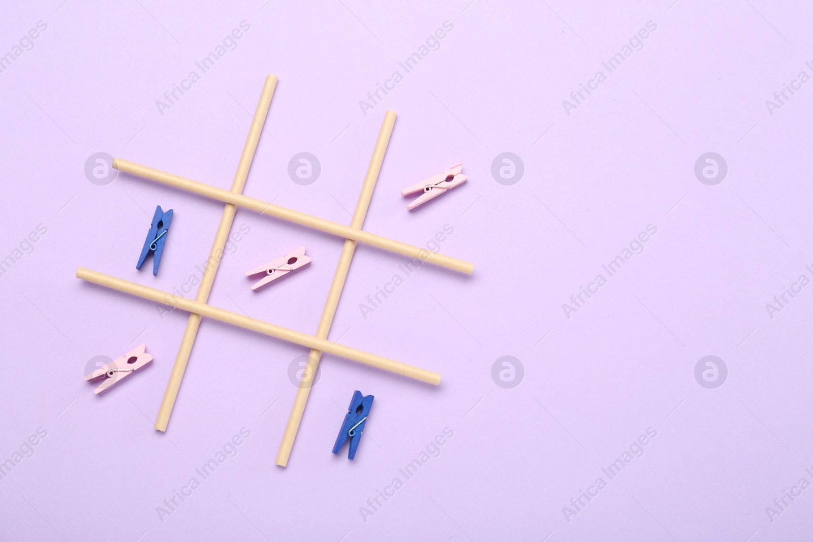 Photo of Tic tac toe game made with clothespins on violet background, top view. Space for text