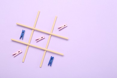 Photo of Tic tac toe game made with clothespins on violet background, top view. Space for text