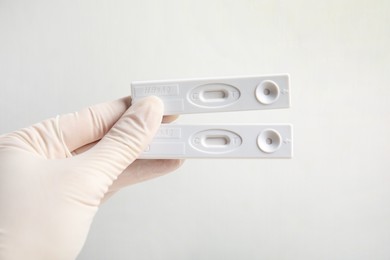 Photo of Doctor in gloves holding disposable express tests for hepatitis on white background, closeup