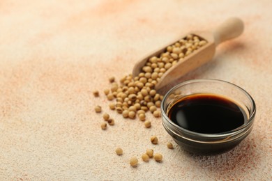 Photo of Soy sauce in bowl and beans on beige textured table, closeup. Space for text