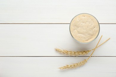 Leaven and ears of wheat on white wooden table, flat lay. Space for text