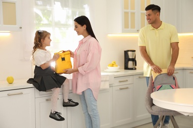 Photo of Parents helping their little child get ready for school in kitchen