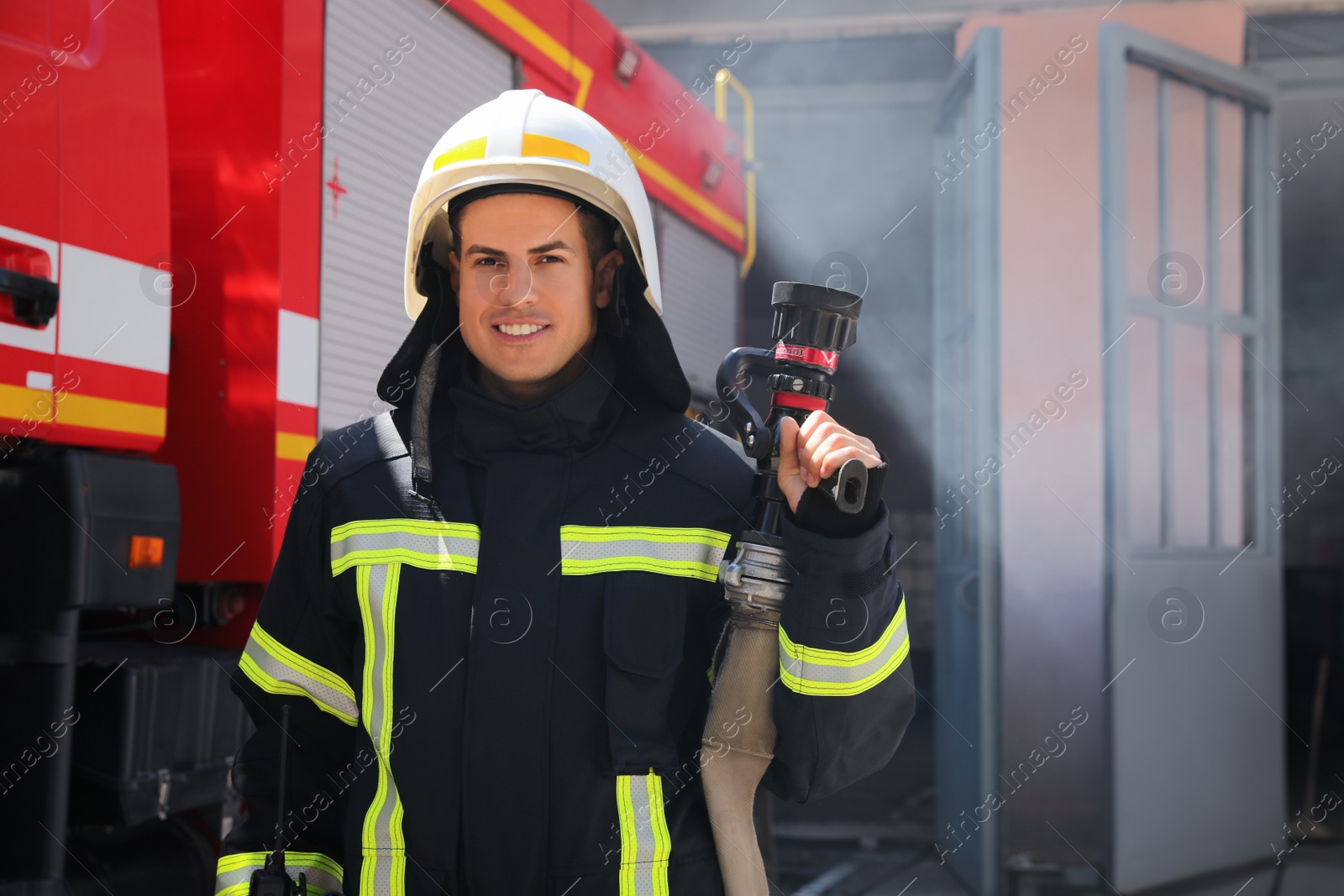 Photo of Portrait of firefighter in uniform with high pressure water jet near fire truck outdoors