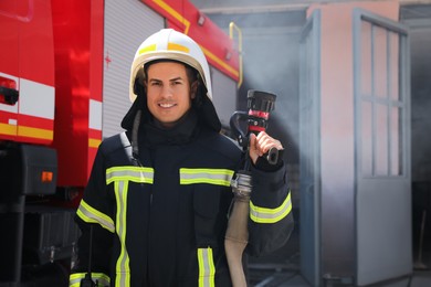 Photo of Portrait of firefighter in uniform with high pressure water jet near fire truck outdoors