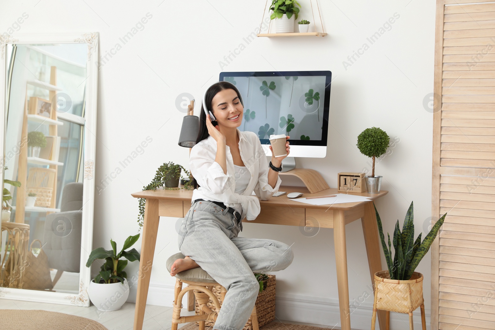 Photo of Young woman with cup of drink at table in room. Home office