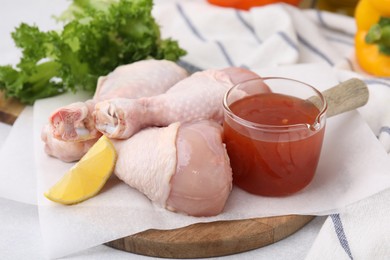 Photo of Fresh marinade, raw chicken drumsticks and lemon wedge on table, closeup
