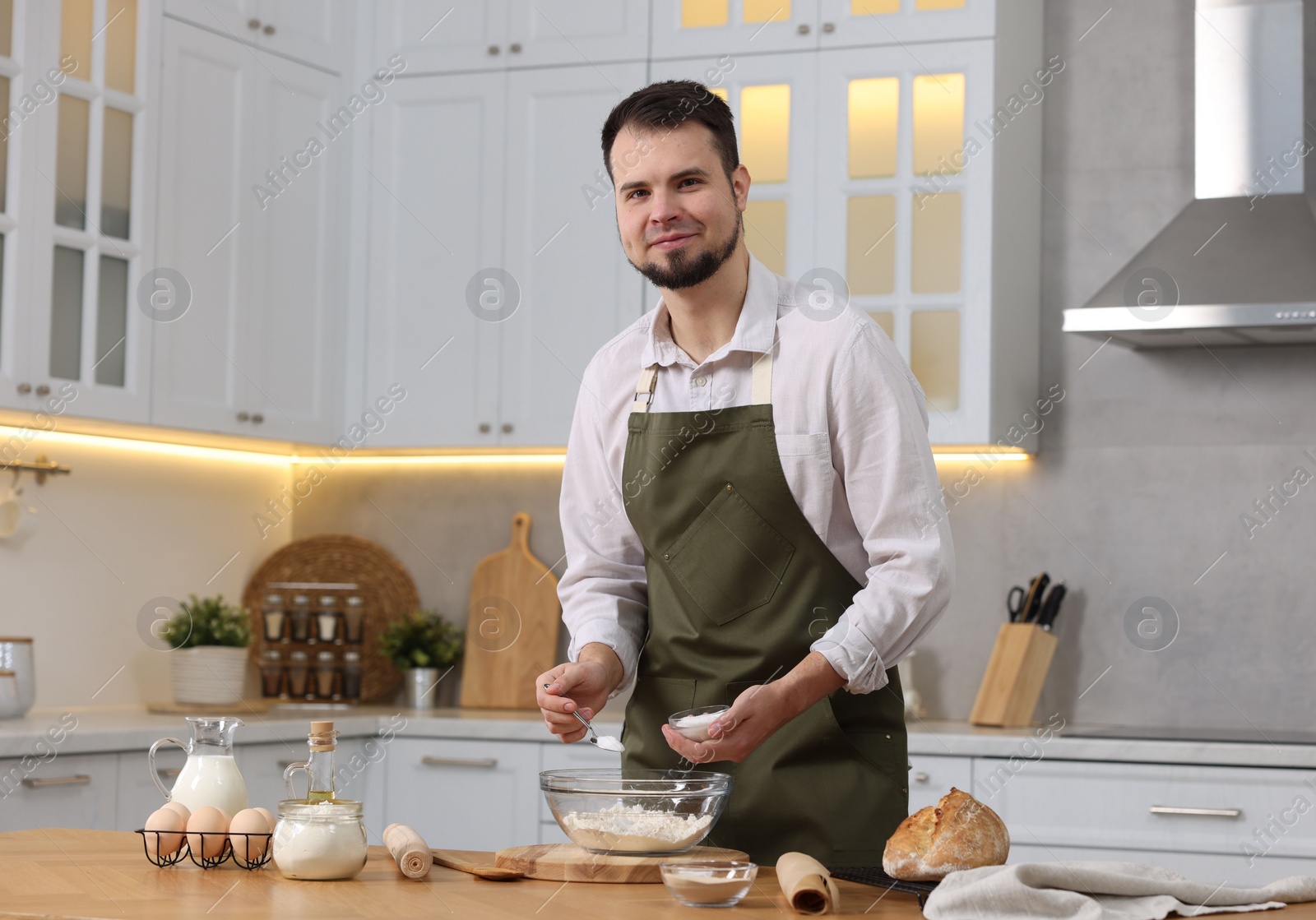 Photo of Making bread. Man putting salt into bowl with flour at wooden table in kitchen