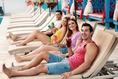 Happy young friends with fresh summer cocktails relaxing on sunbeds