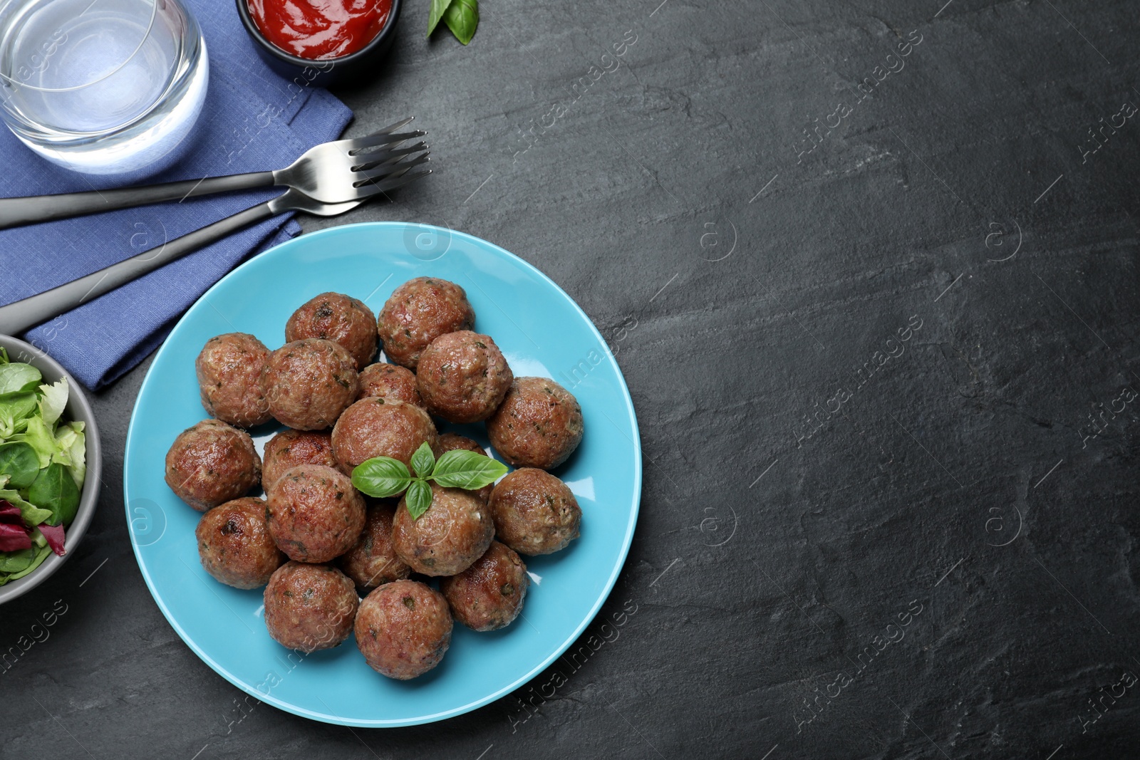 Photo of Tasty cooked meatballs with basil served on black table, flat lay. Space for text