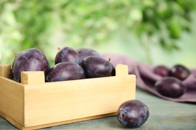 Delicious ripe plums in crate on wooden table against blurred background