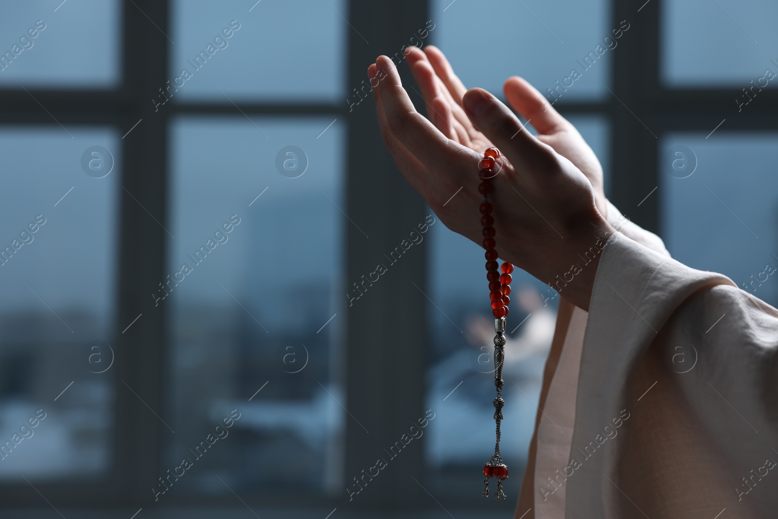 Photo of Muslim man with misbaha praying near window indoors, closeup. Space for text