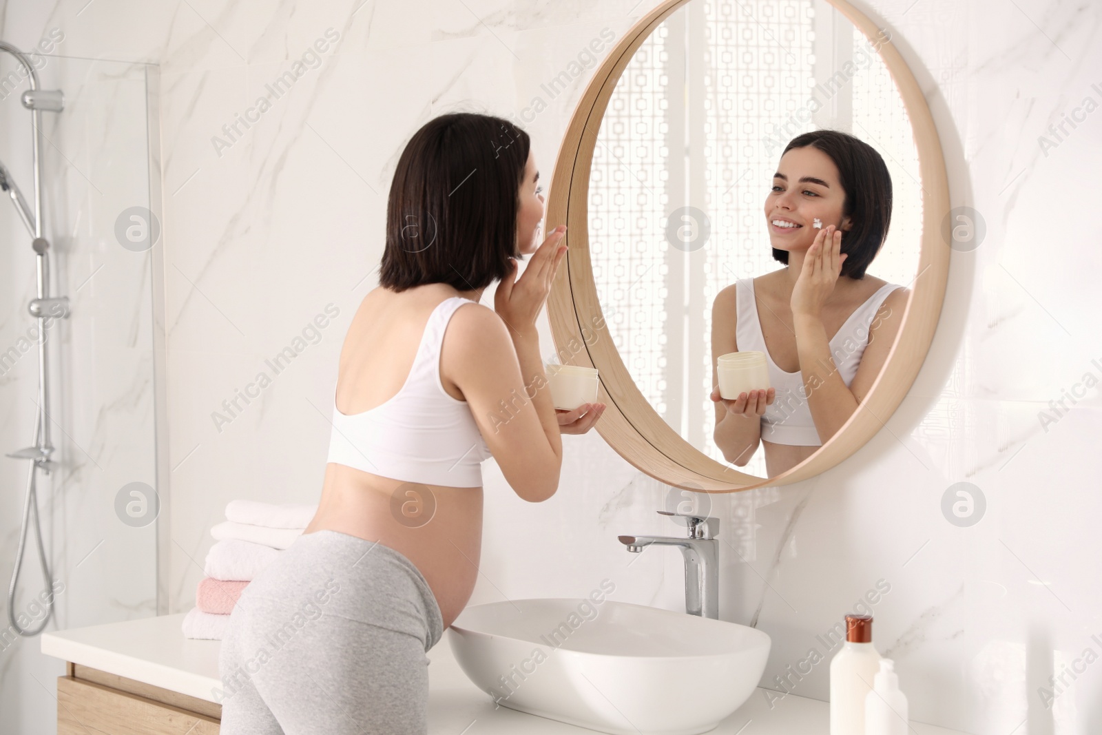 Photo of Young pregnant woman with cosmetic product in bathroom