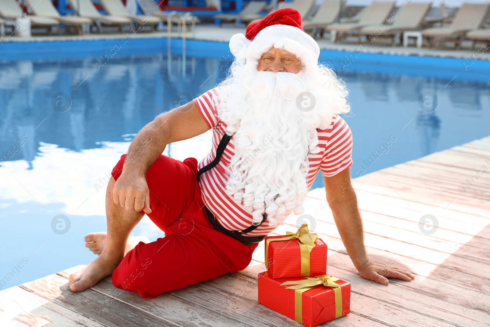 Photo of Authentic Santa Claus with gift boxes near pool at resort