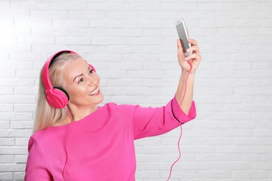 Photo of Mature woman in headphones with mobile device against brick wall