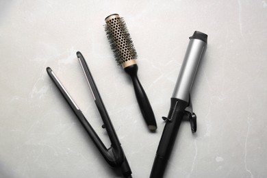 Photo of Hair irons and round brush on light grey marble table, flat lay