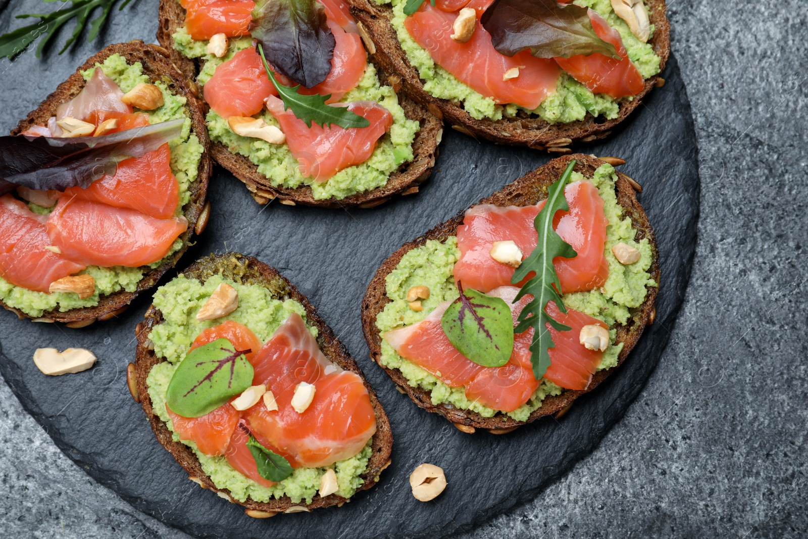 Photo of Delicious sandwiches with salmon, avocado and herbs on grey table, top view