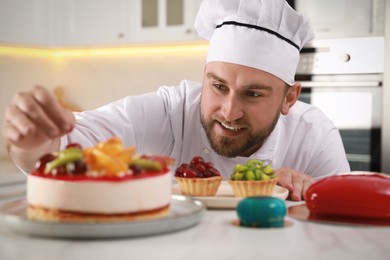 Photo of Happy professional confectioner decorating delicious cake at table in kitchen