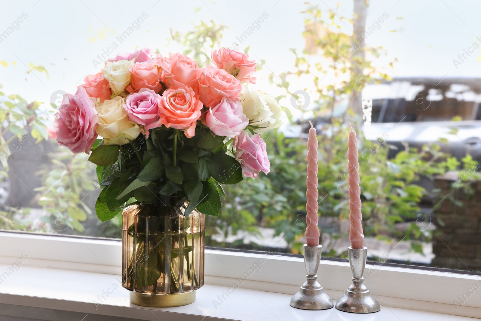 Photo of Vase with beautiful bouquet of roses and candles on windowsill indoors