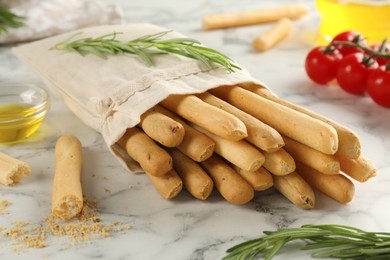 Delicious grissini sticks, oil, rosemary and tomatoes on white marble table, closeup