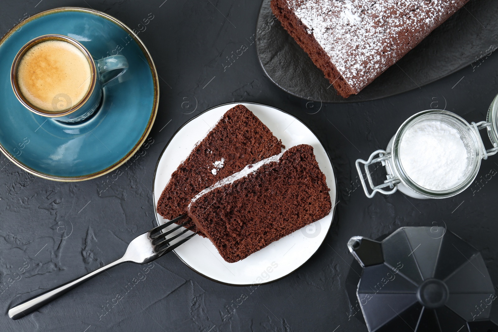 Photo of Tasty chocolate sponge cake with powdered sugar and coffee on black textured table, flat lay