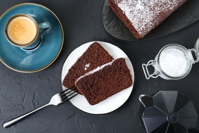 Photo of Tasty chocolate sponge cake with powdered sugar and coffee on black textured table, flat lay