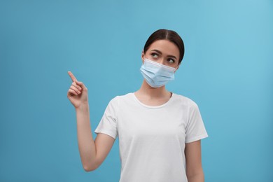 Photo of Woman in medical mask pointing at something on light blue background