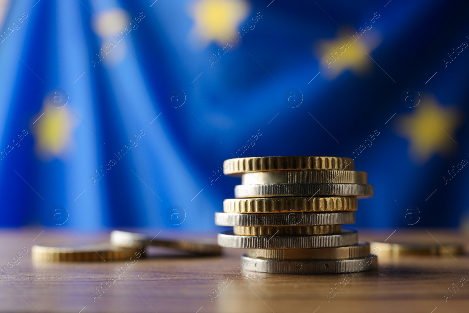 Photo of Coins on wooden table against European Union flag, closeup. Space for text