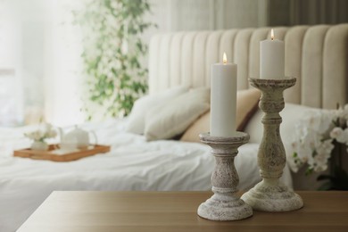 Photo of Pair of beautiful candlesticks on wooden table in bedroom, space for text