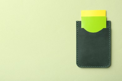 Photo of Leather business card holder with colorful cards on light green background, top view. Space for text