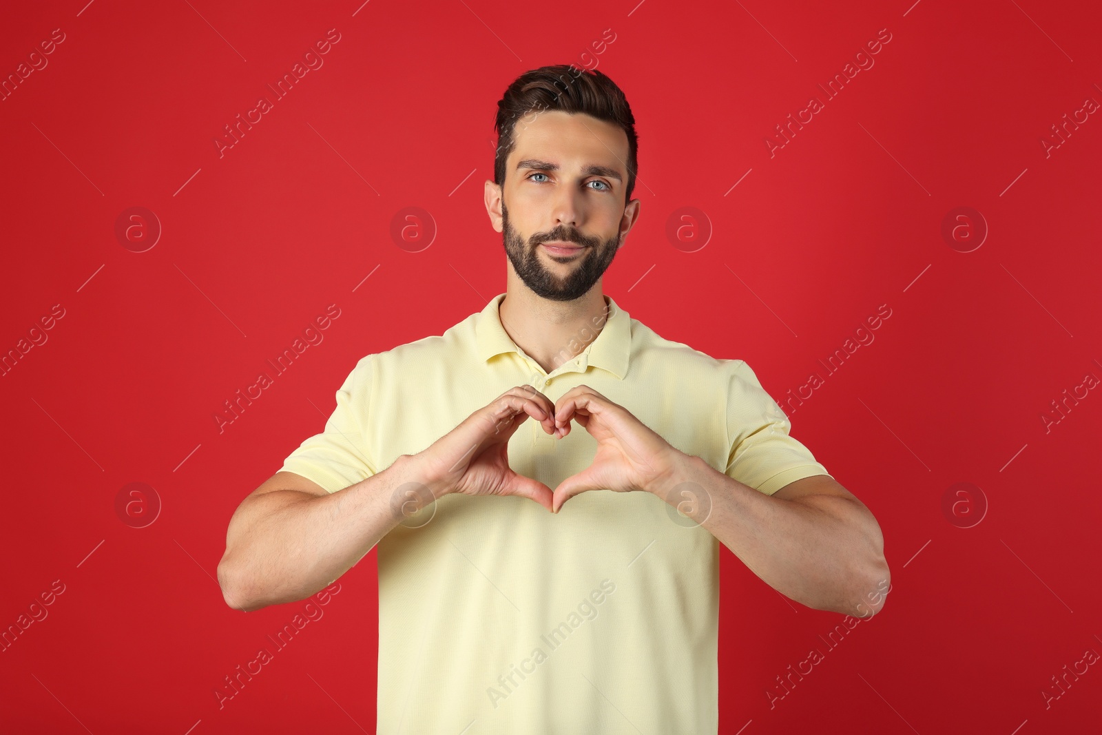 Photo of Man making heart with hands on red background