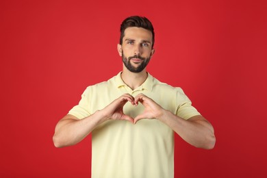 Photo of Man making heart with hands on red background