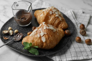 Photo of Delicious croissants with chocolate, nuts and spoon on white marble table