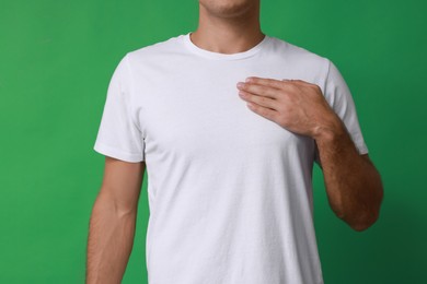 Photo of Man holding hand near chest on green background, closeup