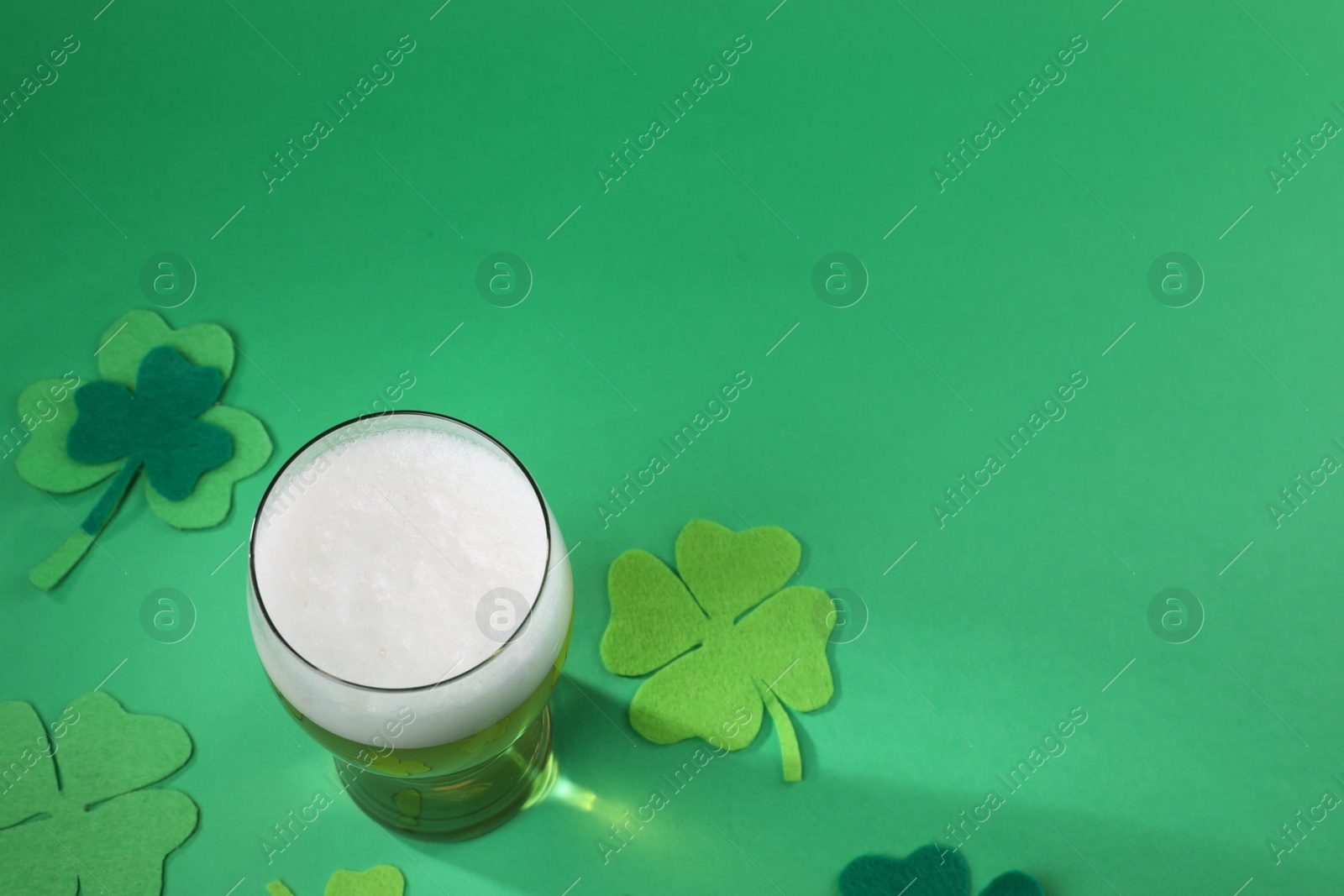 Photo of St. Patrick's day party. Green beer in glass and decorative clover leaves on green background, above view. Space for text