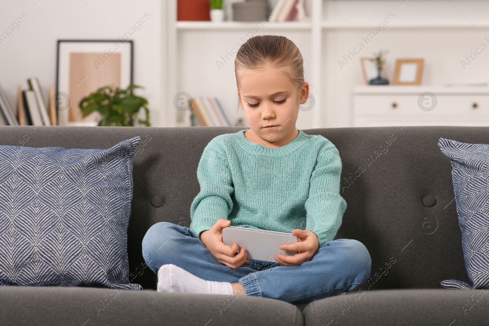 Photo of Little girl using smartphone on sofa at home. Internet addiction