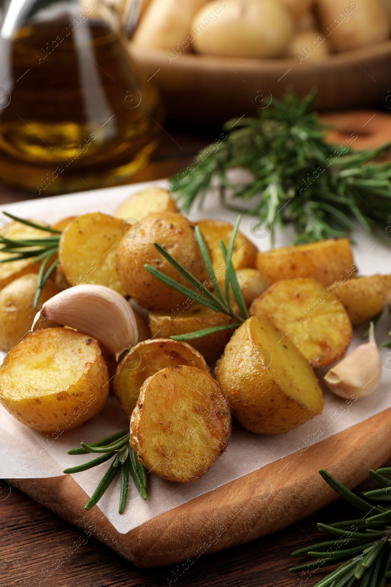 Photo of Delicious baked potatoes with rosemary and garlic on parchment paper, closeup