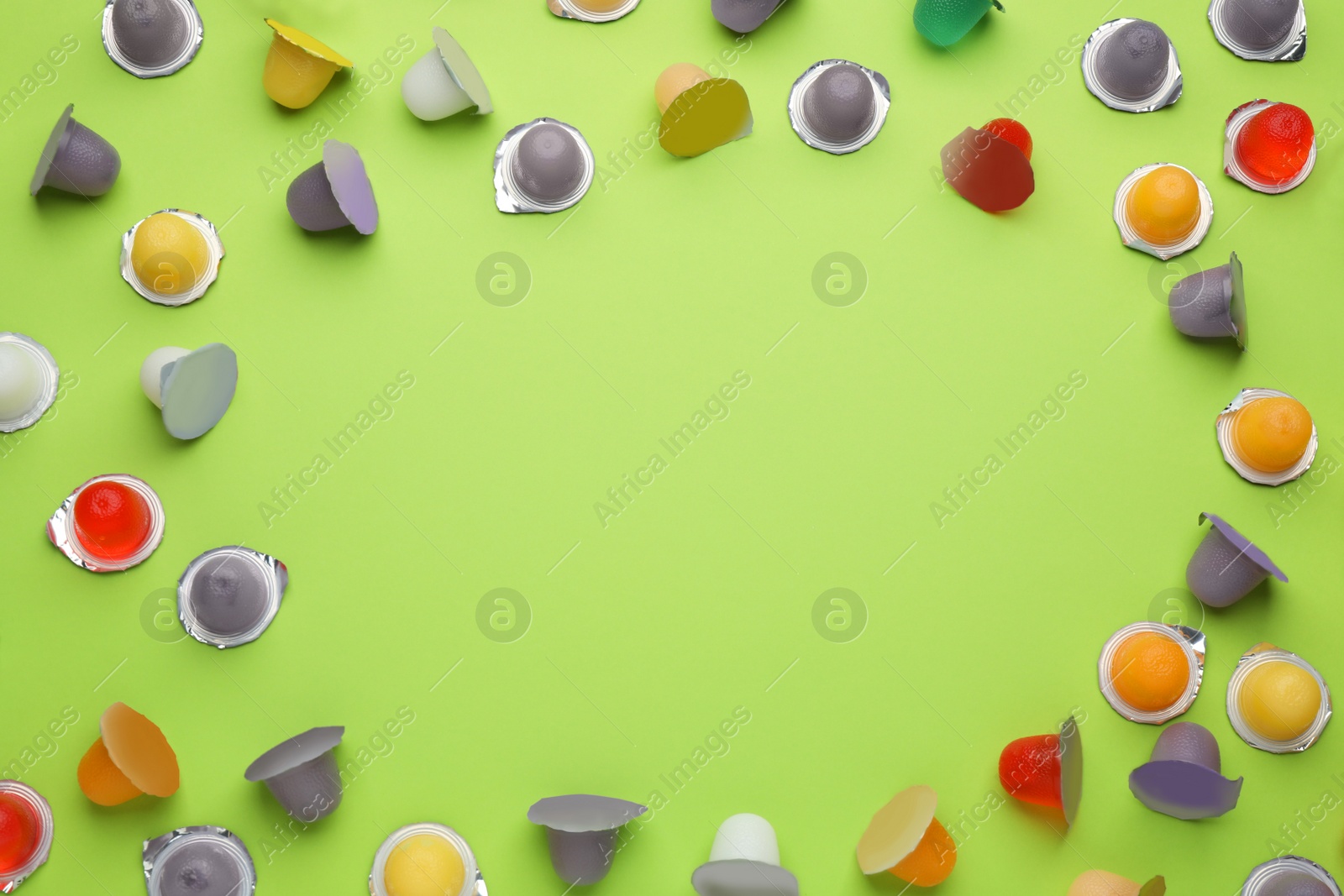 Photo of Frame of tasty bright jelly cups on green background, flat lay. Space for text